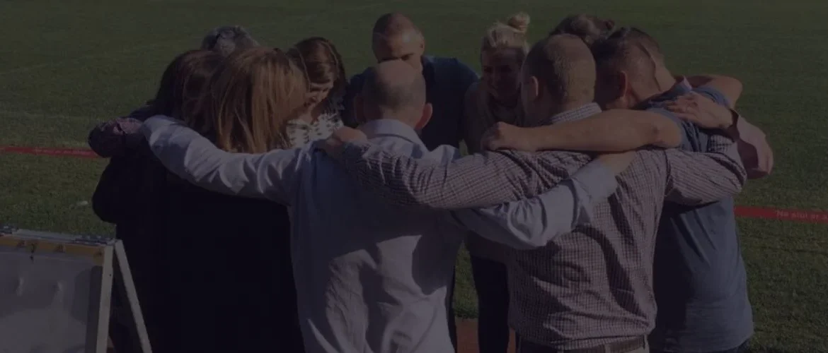 Corporate team in a group huddle, expressing unity and motivation outdoors.