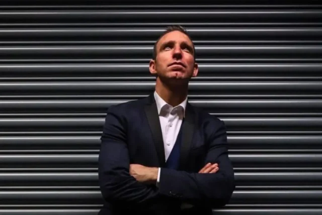 Author Enda McNulty standing with arms crossed in front of a metal shutter, looking upwards.