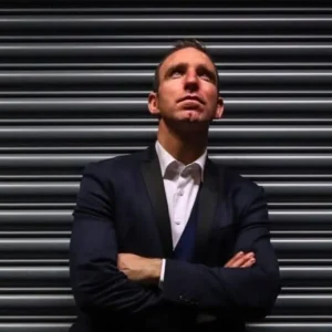 Author Enda McNulty standing with arms crossed in front of a metal shutter, looking upwards.