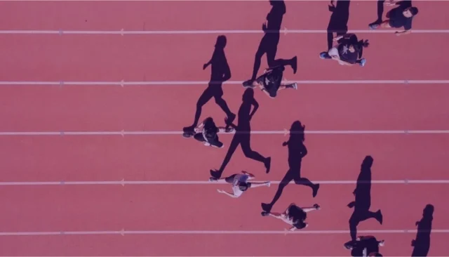 Aerial view of a pink running track with shadows of runners in motion, depicting teamwork and competitive spirit.