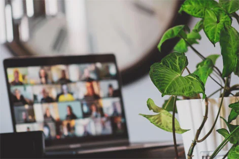 Laptop screen displaying a virtual meeting with multiple participants, placed beside a vibrant indoor plant, symbolising a remote work environment.
