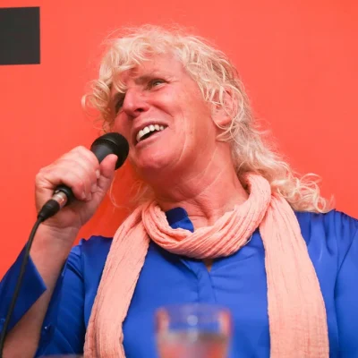 Speaker with curly blonde hair laughing joyfully while speaking at the Commit 2 Lead event.