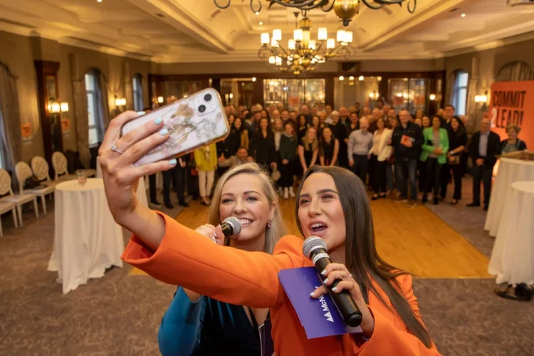 Two presenters taking a selfie with the audience at the Commit 2 Lead event.