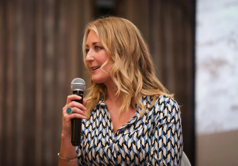 Blonde woman speaking at Commit 2 Lead event, patterned blue and white blouse.