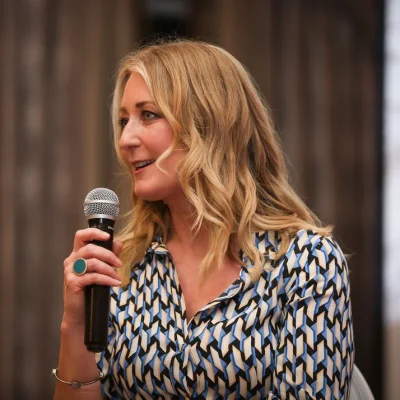 Blonde woman speaking at Commit 2 Lead event, patterned blue and white blouse.