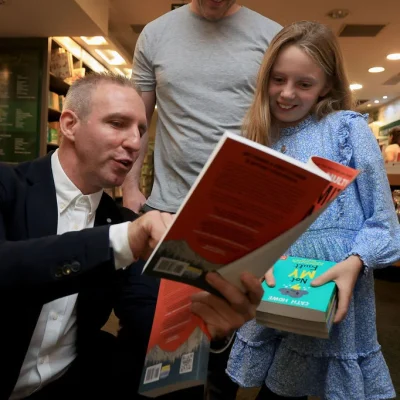 Author showing a book to a young girl, with a man observing at a bookshop event.