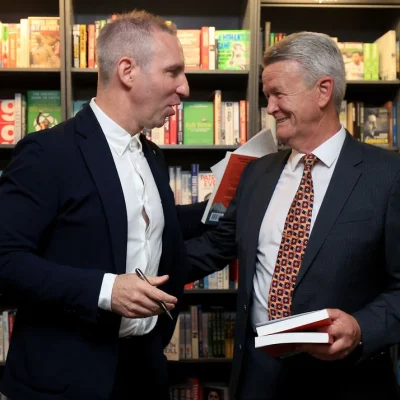 Author in deep conversation with a male attendee holding a book in a bookshop.