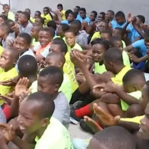 Large group of children clapping and sitting outside, enjoying a community event.