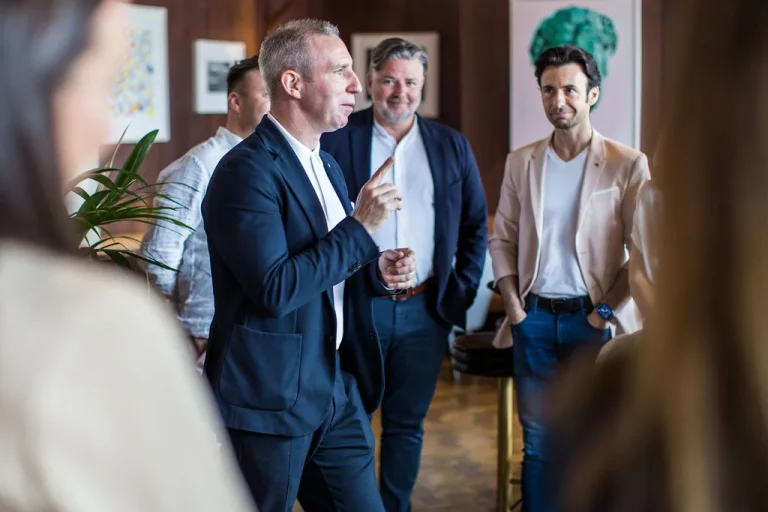 Professional speaker addressing an audience during a client event with engaged listeners in the background.