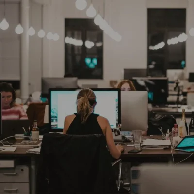 Office scene captured in a lower-light setting, showing various employees engaged at their workstations, highlighting a productive and focused atmosphere.