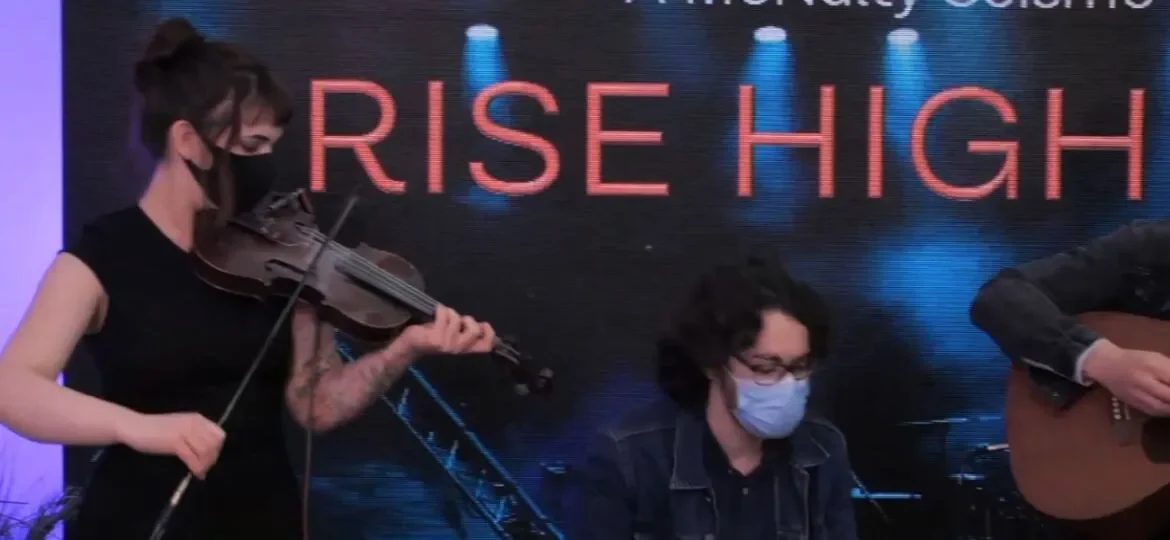 Musicians performing live, one playing violin and the other guitar, in the Rise Higher event.