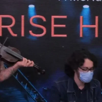 Musicians performing live, one playing violin and the other guitar, in the Rise Higher event.