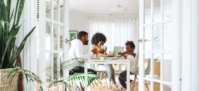 Family engaging in a meal together in a brightly-lit, plant-filled modern dining room, reflecting a harmonious work-life balance.