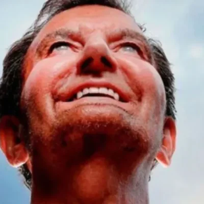 Alan Kelly looking upwards with a smile, raising his hands, against a background of a blue sky.