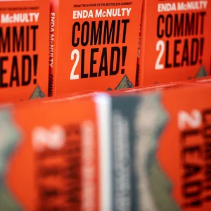 Multiple copies of the book 'Commit 2 Lead!' by Enda McNulty displayed on a table at an event.