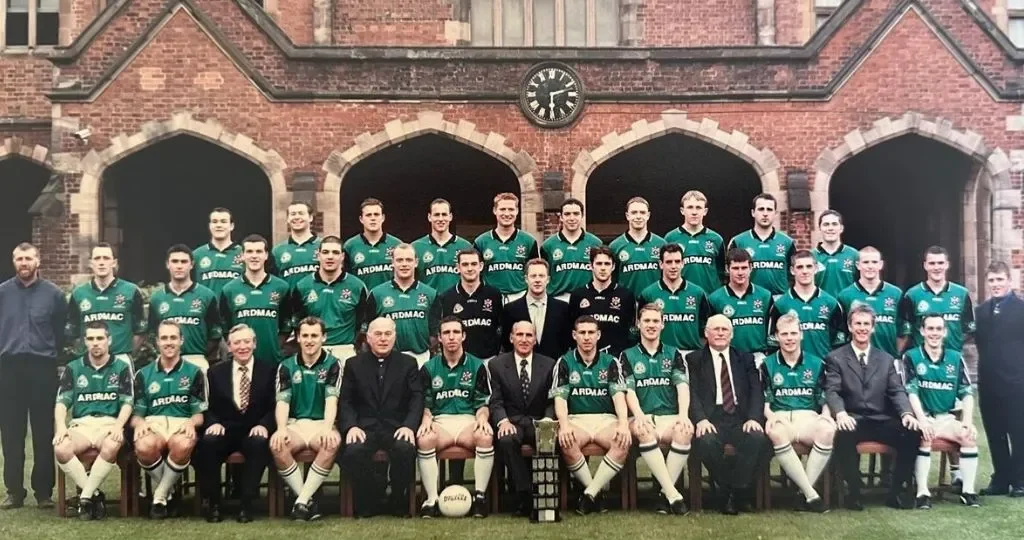 Group photo of the Queen's University Gaelic Football team standing in front of a historic building, showcasing players and coaching staff.